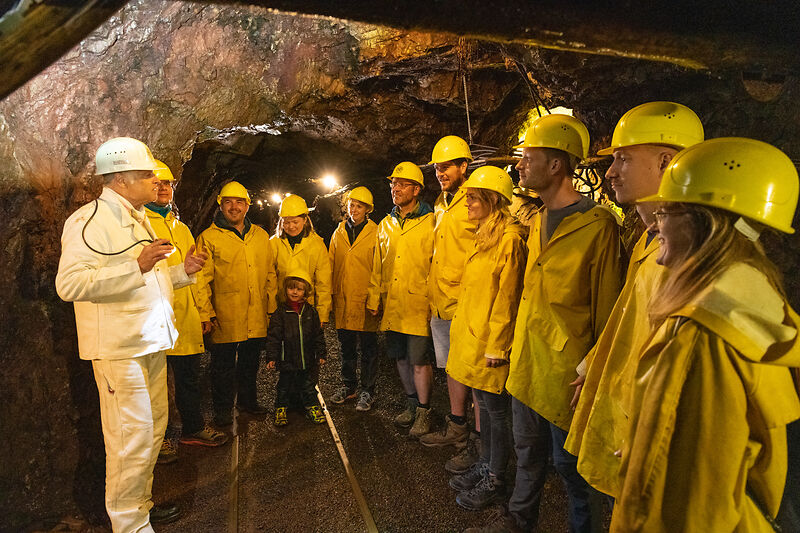 Gruppe von Besuchern in gelben Mänteln und gelben Helmen im Stollen