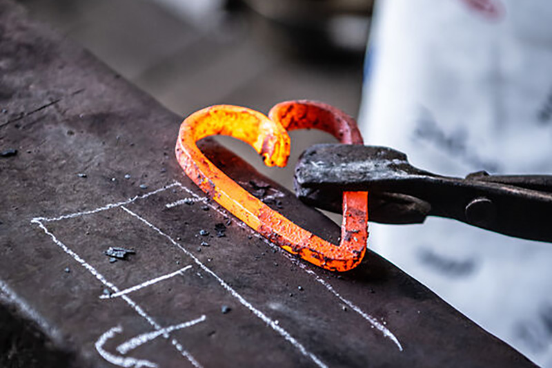 Rot glühendes, geschmiedetes Eisen in Form eines Herzens, welches von einer Zange gehalten wird